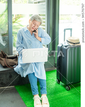 relax, vacation, travel, portrait of senior adult elderly asian woman 60s smiling using the computer laptop and smartphone while waiting for their travel time. relax, vacation, travel, portrait of senior adult elderly asian woman 60s smiling using the computer laptop and smartphone while waiting for their travel time. 94570797