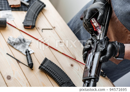 Close up of a man in apron lubricates the mechanism of the weapon with oil Close up of a man in apron lubricates the mechanism of the weapon with oil 94571695