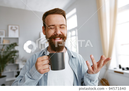 Young bearded man smiling and drinking coffee at home 94571840
