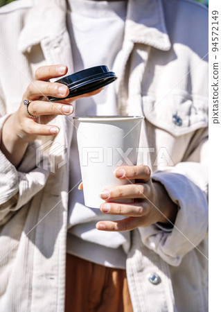 Girl with a cup of takeaway coffee. Stylish girl holding paper cup with hot drink outdoors. Lifestyle concept 94572149