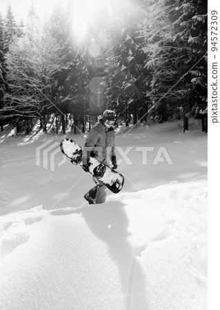 Freerider with snowboard in hands at snowy spruce forest. Black and white. 94572309