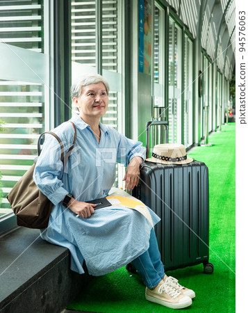 休閒、度假、旅行，60歲的亞洲女性面帶微笑，坐在手提包裡，提著包等，等待著旅行的時間。 94576063