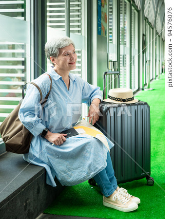 休閒、度假、旅行,60歲的亞洲女性面帶微笑,坐在手提包裡,提著包等,等待著旅行的時間。 休閒、度假、旅行,60歲的亞洲女性面帶微笑,坐在手提包裡,提著包等,等待著旅行的時間。 94576076