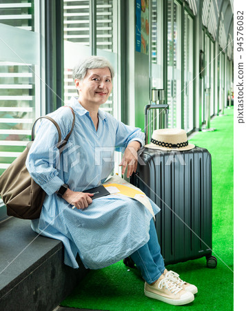 休閒、度假、旅行，60歲的亞洲女性面帶微笑，坐在手提包裡，提著包等，等待著旅行的時間。 94576082