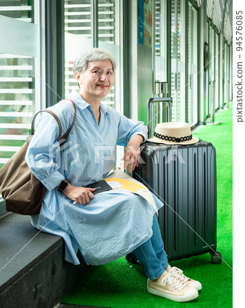 休閒、度假、旅行,60歲的亞洲女性面帶微笑,坐在手提包裡,提著包等,等待著旅行的時間。 休閒、度假、旅行,60歲的亞洲女性面帶微笑,坐在手提包裡,提著包等,等待著旅行的時間。 94576085