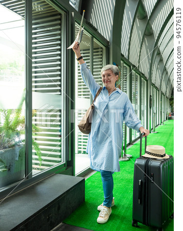 60歲亞洲老太婆畫像,面帶微笑,駐紮,手提箱,手持旗桿,靈活的旅行樂隊概念。 60歲亞洲老太婆畫像,面帶微笑,駐紮,手提箱,手持旗桿,靈活的旅行樂隊概念。 94576119