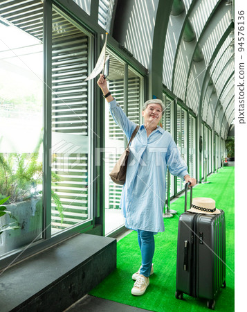60歲亞洲老太婆畫像，面帶微笑，駐紮，手提箱，手持旗桿，靈活的旅行樂隊概念。 94576136