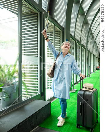 60歲亞洲老太婆畫像，面帶微笑，駐紮，手提箱，手持旗桿，靈活的旅行樂隊概念。 94576139