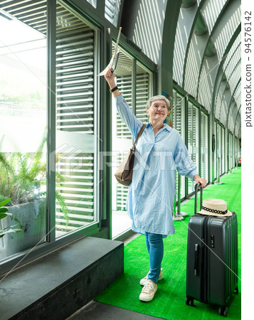 60歲亞洲老太婆畫像，面帶微笑，駐紮，手提箱，手持旗桿，靈活的旅行樂隊概念。 94576142