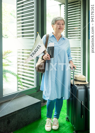 60歲亞洲老太婆畫像，面帶微笑，駐紮，手提箱，手持旗桿，靈活的旅行樂隊概念。 94576161