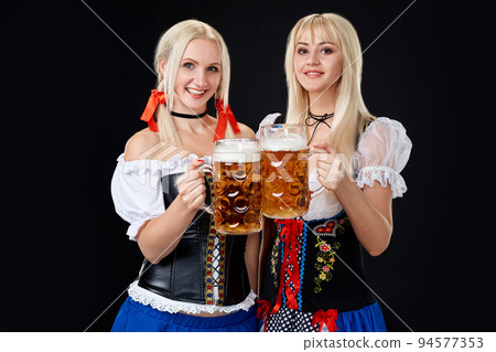 Young and beautiful bavarian girls with two beer mugs on black background 94577353