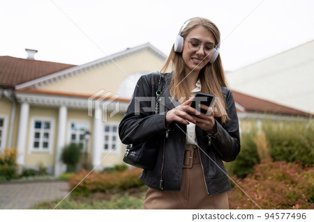 young woman goes to work listening to music in headphones via mobile phone young woman goes to work listening to music in headphones via mobile phone 94577496