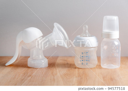 Manual breast pump and nursing bottles for newborn baby on wooden table. Device for increasing milk supply for breastfeeding mother. Maternity, baby care concept. Manual breast pump and nursing bottles for newborn baby on wooden table. Device for increasing milk supply for breastfeeding mother. Maternity, baby care concept. 94577518