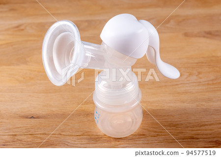 Manual breast pump on wooden table. Device for increasing milk supply for breastfeeding mother. Maternity and baby care concept Manual breast pump on wooden table. Device for increasing milk supply for breastfeeding mother. Maternity and baby care concept 94577519
