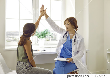 Cheerful young female doctor gives high five to teenage girl after medical examination. 94577548
