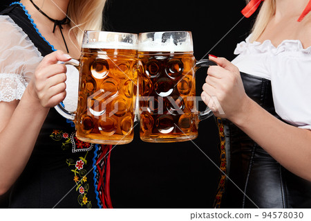 Young and beautiful bavarian girls with two beer mugs on black background 94578030