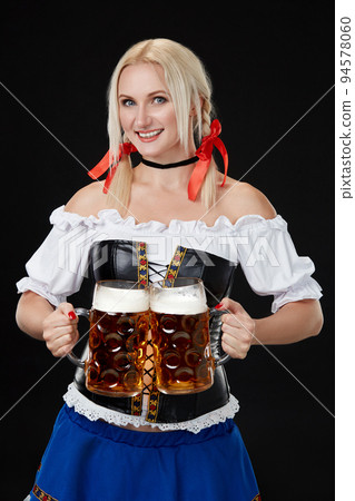 Young sexy woman wearing a dirndl with two beer mugs on black background Young sexy woman wearing a dirndl with two beer mugs on black background 94578060