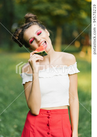 A smiling girl holds a sweet watermelon in her hands and smiles while biting it A smiling girl holds a sweet watermelon in her hands and smiles while biting it 94578219