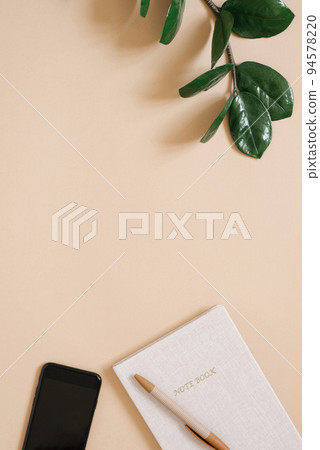 Desktop of a designer or blogger. A table with a phone, a pen and Notepad, and a branch of a green zamiokulkas plant. Top view with copy space, flat lay 94578220