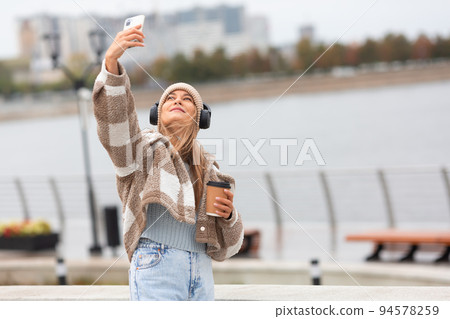 Photo of a young woman taking a selfie with her smartphone during outdoor walk. Photo of a young woman taking a selfie with her smartphone during outdoor walk. 94578259
