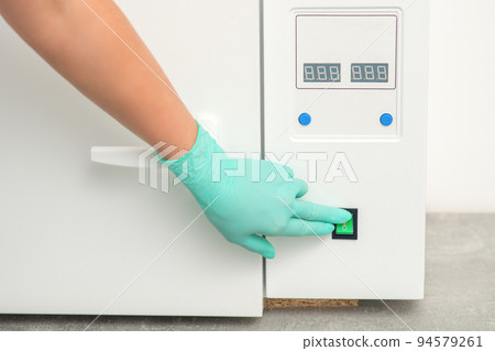 Beautician in protective gloves starts the machine for disinfection of tools before the medical procedure 94579261