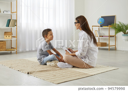 Female school counseling psychologist is talking to smart little boy during therapy session. 94579998