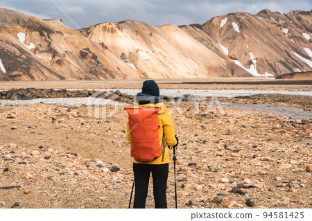 Female backpacker in yellow jacket standing in Landmannalaugar trail on Icelandic highlands in summer at Iceland 94581425