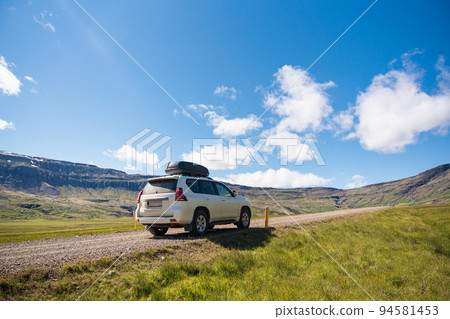 Large car parked on dirt road among the mountain and meadow on sunny day in summer Large car parked on dirt road among the mountain and meadow on sunny day in summer 94581453