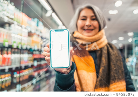 Senior woman at the supermarket shows the screen of her smartphone 94583072