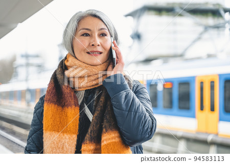 Senior woman send message with a mobile phone and waits for a train 94583113