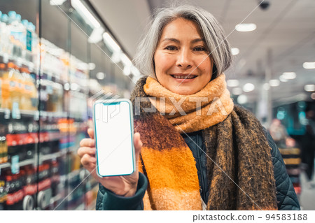 Senior woman at the supermarket shows the screen of her smartphone 94583188