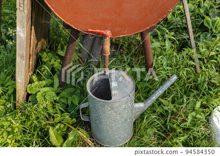 Rain barrel and watering can in vegetable garden. Watering the garden during a drought. Rain barrel and watering can in vegetable garden. Watering the garden during a drought. 94584350