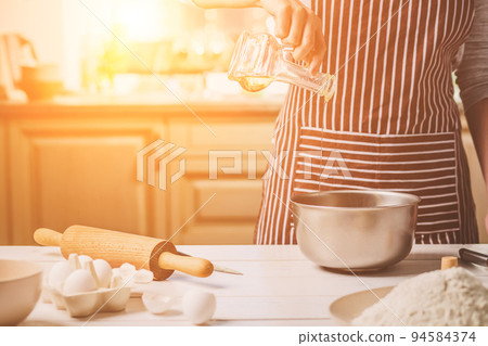 Young woman pouring oil into a bowl with dough, close-up 94584374