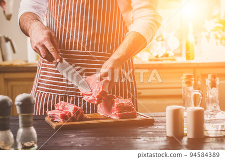 Man cuts of fresh piece of beef on a wooden cutting board in the home kitchen 94584389