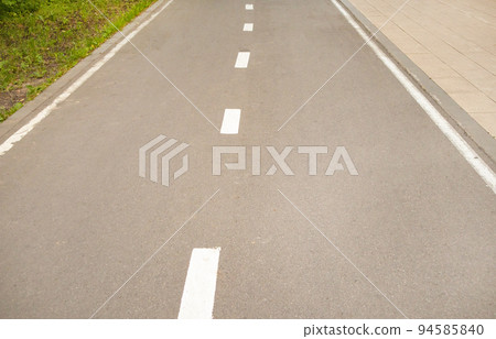 Close-up of an asphalt road with an intermittent marking line and grass on the side of the road. Selective focus, black and white photography 94585840