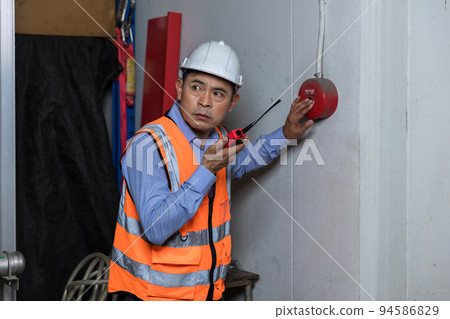 Foreman or worker pushing fire alarm on the wall. 94586829