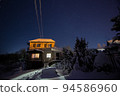Night shot of a countryside brick house with lighted windows with a starry sky on a background in winter. Concept of peace, magic, idyllic, home, dreams. 94586960
