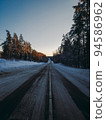 Country snowy road through coniferous forest in winter. Sunset 94586962