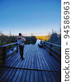 Young woman standing on a wooden pier and taking photo of a large crayfish lake. State Natural Reserve Cancer Lakes , St. Petersburg 94586963