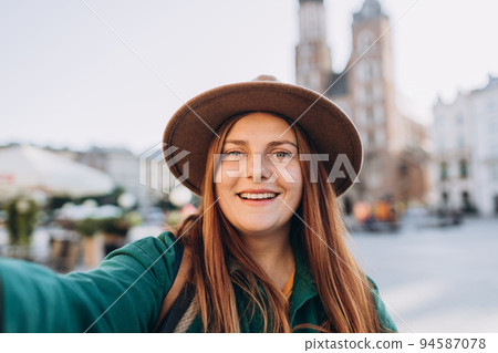 Young woman tourist in hat making selfie photo in front of the famous St. Mary's Basilica on the Market square in Krakow, Poland. Traveling Europe in autumn. 94587078