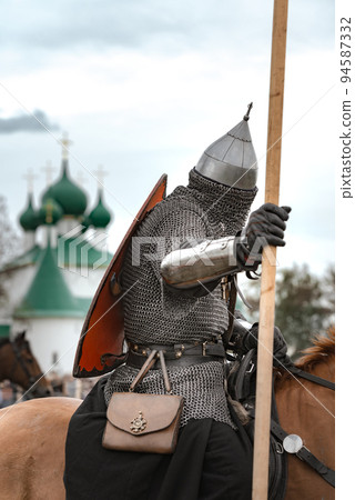 Horseman in chain mail armor, helmet and shield on a robe on horse on a background of church 94587332