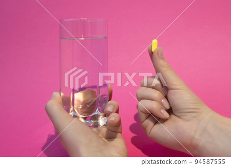 Female hands hold a glass of water and a pill on a pink background. Health and medicine. Female hands hold a glass of water and a pill on a pink background. Health and medicine. 94587555