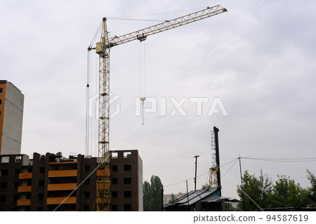 A crane builds a house at a height, lifts the load to the upper floor. The construction site of a residential building, a building against the sky. High quality photo 94587619
