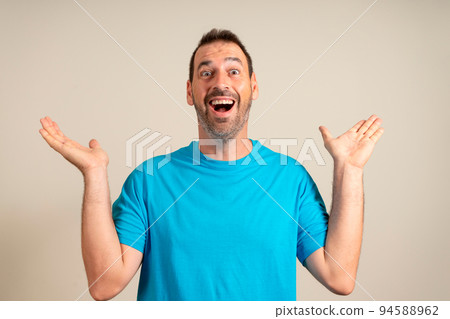 Funny smiling man in blue t-shirt showing palms up, unexpected surprise gesture isolated on beige background. Attractive happy man hearing good news, catching something 94588962