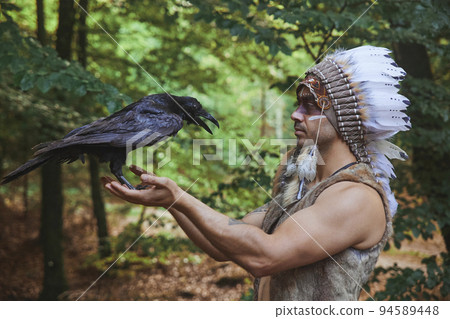 A man in traditional Native American clothing holding a crow  94589448