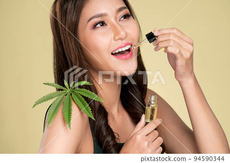 Young ardent woman with healthy skin holding taking cbd oil hemp leaf. 94590344