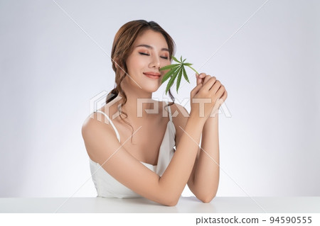 Gorgeous female model with healthy fresh skin and cosmetic holding hemp leaf. Gorgeous female model with healthy fresh skin and cosmetic holding hemp leaf. 94590555