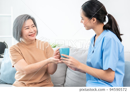 Female care taker serving her contented senior patient with a cup of coffee. Female care taker serving her contented senior patient with a cup of coffee. 94590572