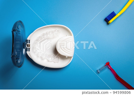 white special container box for invisible plastic braces, aligners, with a toothbrush and an orthodontic brush lies on a blue background 94599806
