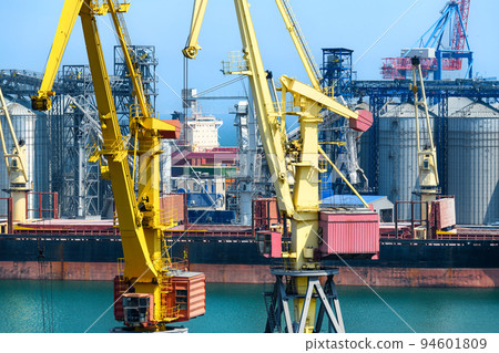 industrial seaport infrastructure, sea, cranes and dry cargo ship, grain silo, bulk carrier vessel and grain storage elevators, concept of sea cargo transportation 94601809